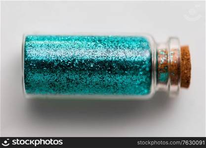 party, decoration and holidays concept - blue glitters in small glass bottle with cork stopper over white background. blue glitters in bottle over white background