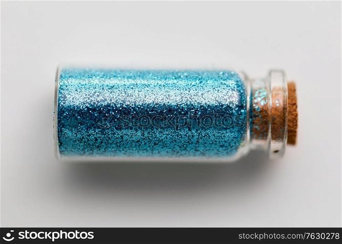 party, decoration and holidays concept - blue glitters in small glass bottle with cork stopper over white background. blue glitters in bottle over white background