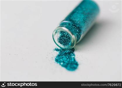 party, decoration and holidays concept - close up of blue glitters poured from small glass bottle over white background. blue glitters poured from small glass bottle