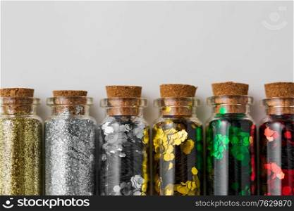 party, decoration and holidays concept - close up of different color glitters in small glass bottles with cork stoppers over white background. set of glitters in bottles over white background