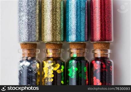 party, decoration and holidays concept - close up of different color glitters in small glass bottles with cork stoppers over white background. set of glitters in bottles over white background