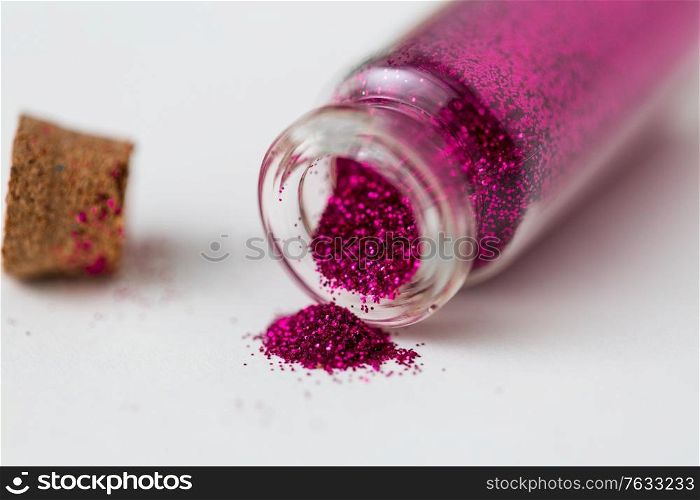 party, decoration and holidays concept - close up of fuchsia pink glitters poured from small glass bottle and cork over white background. pink glitters poured from small glass bottle