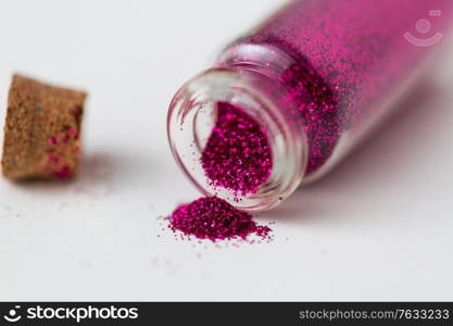 party, decoration and holidays concept - close up of fuchsia pink glitters poured from small glass bottle and cork over white background. pink glitters poured from small glass bottle