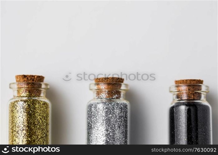 party, decoration and holidays concept - close up of gold, silver and black metallic glitters in small glass bottles with cork stoppers over white background. set of glitters in bottles over white background