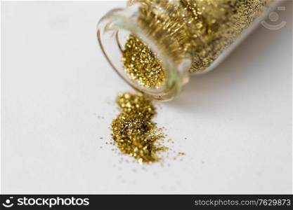 party, decoration and holidays concept - close up of golden glitters poured from small glass bottle over white background. golden glitters poured from small glass bottle