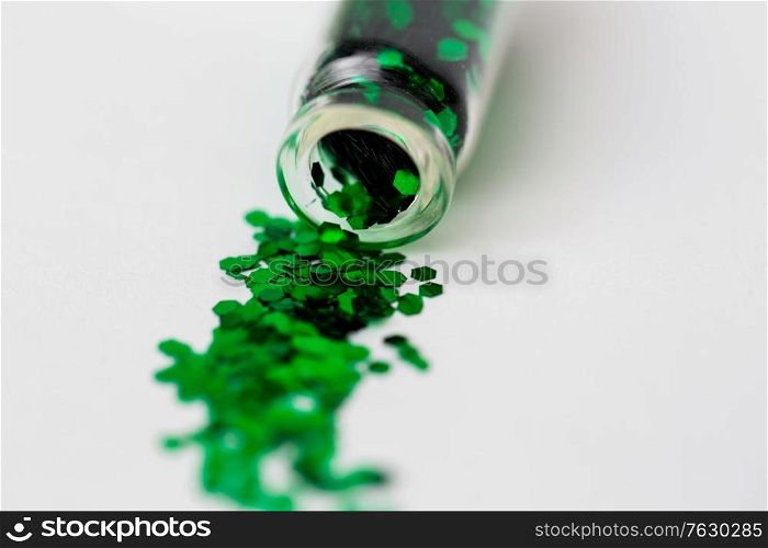 party, decoration and holidays concept - close up of green hexagonal glitters poured from small glass bottle over white background. green glitters poured from small glass bottle
