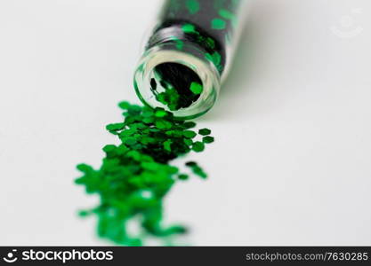 party, decoration and holidays concept - close up of green hexagonal glitters poured from small glass bottle over white background. green glitters poured from small glass bottle