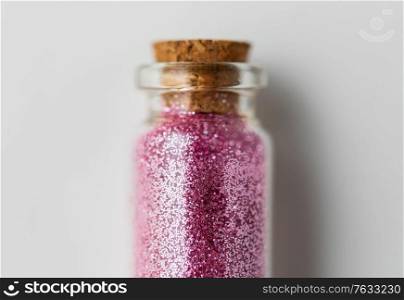 party, decoration and holidays concept - close up of pink glitters in small glass bottle with cork stopper over white background. pink glitters in bottle over white background