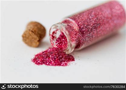 party, decoration and holidays concept - close up of pink red glitters poured from small glass bottle and cork over white background. pink red glitters poured from small glass bottle