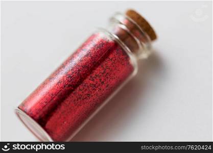 party, decoration and holidays concept - close up of red glitters in small glass bottle with cork stopper over white background. red glitters in bottle over white background