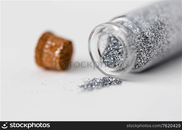 party, decoration and holidays concept - close up of silver glitters poured from small glass bottle and cork over white background. silver glitters poured from small glass bottle