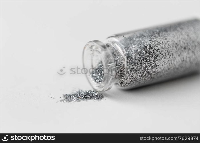 party, decoration and holidays concept - close up of silver glitters poured from small glass bottle over white background. silver glitters poured from small glass bottle