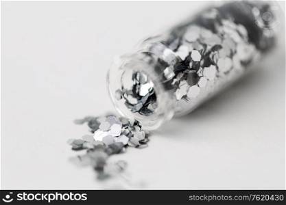 party, decoration and holidays concept - close up of silver hexagonal glitters poured from small glass bottle over white background. silver glitters poured from small glass bottle