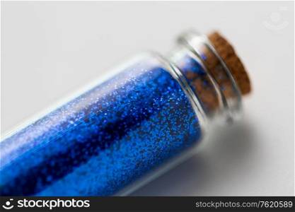 party, decoration and holidays concept - close up of ultramarine blue glitters in small glass bottle with cork stopper over white background. blue glitters in bottle over white background