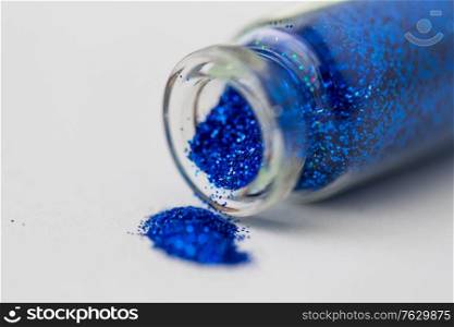 party, decoration and holidays concept - close up of ultramarine blue glitters poured from small glass bottle over white background. blue glitters poured from small glass bottle