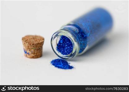 party, decoration and holidays concept - close up of ultramarine blue glitters poured from small glass bottle and cork stopper over white background. blue glitters poured from small glass bottle