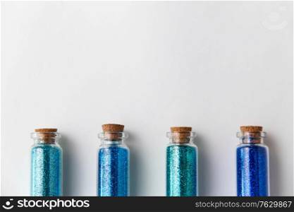 party, decoration and holidays concept - glitters of different blue shades in small glass bottles with cork stoppers over white background. blue glitters in bottles over white background