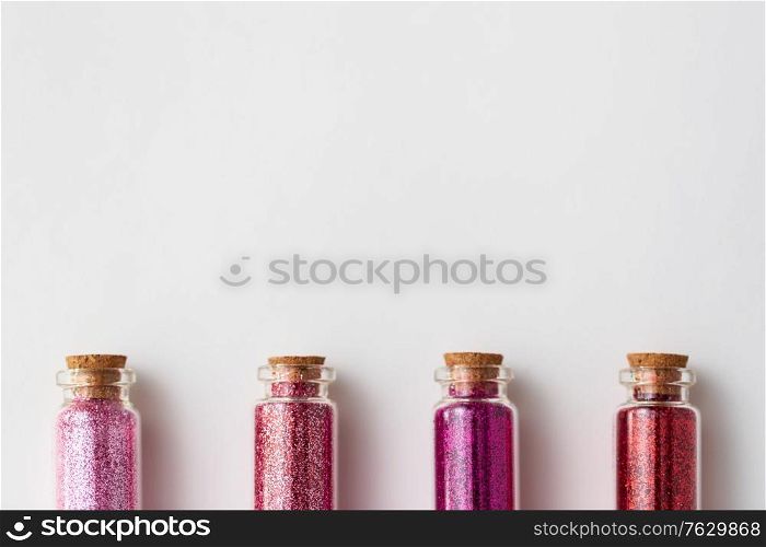 party, decoration and holidays concept - glitters of different red and pink shades in small glass bottles with cork stoppers over white background. red glitters in bottles over white background