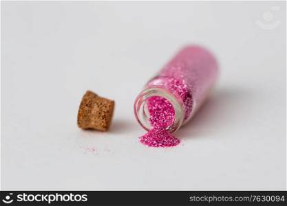 party, decoration and holidays concept - pink glitters poured from small glass bottle and cork over white background. pink glitters poured from small glass bottle