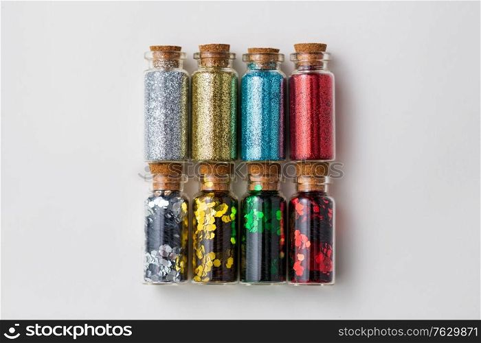 party, decoration and holidays concept - set of different color glitters in small glass bottles with cork stoppers over white background. set of glitters in bottles over white background
