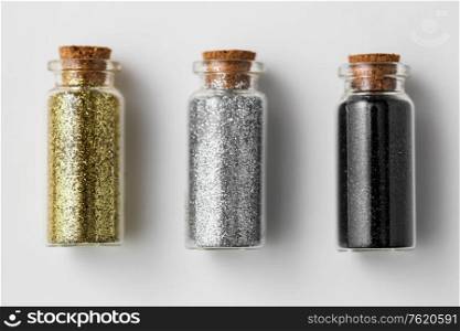party, decoration and holidays concept - set of gold, silver and black metallic glitters in small glass bottles with cork stoppers over white background. set of glitters in bottles over white background