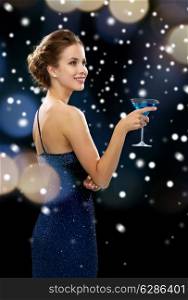 party, drinks, holidays, christmas and people concept - smiling woman in evening dress holding cocktail over night lights and snow background