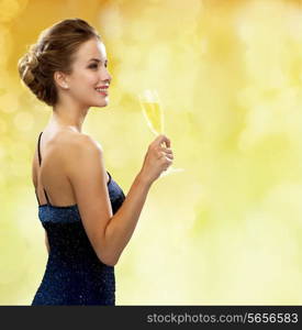 party, drinks, holidays, luxury and celebration concept - smiling woman in evening dress with glass of sparkling wine over yellow lights background