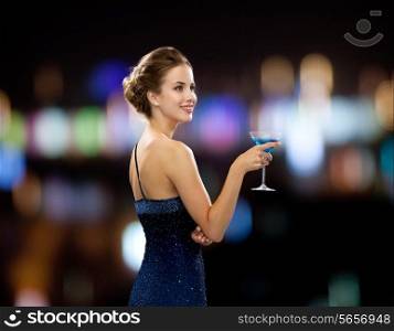 party, drinks, holidays, luxury and celebration concept - smiling woman in evening dress holding cocktail over night lights background