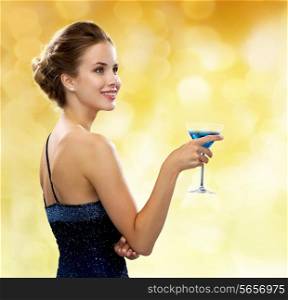 party, drinks, holidays, luxury and celebration concept - smiling woman in evening dress holding cocktail over yellow lights background