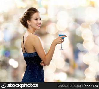 party, drinks, holidays, luxury and celebration concept - smiling woman in evening dress holding cocktail over lights background