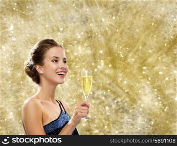 party, drinks, holidays, luxury and celebration concept - smiling woman in evening dress with glass of sparkling wine over yellow lights background