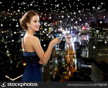 party, drinks, holidays, luxury and celebration concept - smiling woman in evening dress holding cocktail over snowy night city background