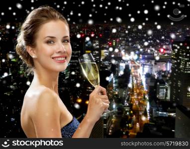 party, drinks, holidays, luxury and celebration concept - smiling woman in evening dress with glass of sparkling wine over snowy night city background
