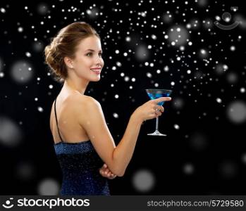 party, drinks, holidays, luxury and celebration concept - smiling woman in evening dress holding cocktail over black snowy background