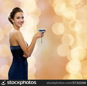 party, drinks, holidays, luxury and celebration concept - smiling woman in evening dress holding cocktail over beige lights background