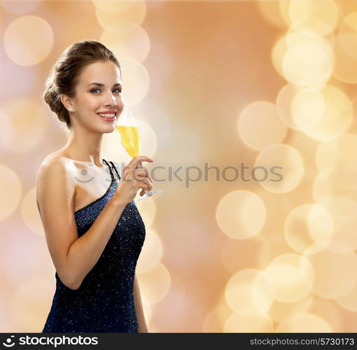 party, drinks, holidays, luxury and celebration concept - smiling woman in evening dress with glass of sparkling wine over beige lights background