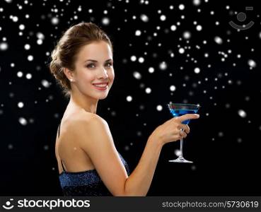 party, drinks, holidays, luxury and celebration concept - smiling woman in evening dress holding cocktail over black snowy background