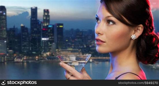 party, drinks, holidays, luxury and celebration concept - smiling woman in evening dress holding cocktail over night city background