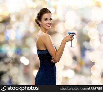 party, drinks, holidays, luxury and celebration concept - smiling woman in evening dress holding cocktail over lights background