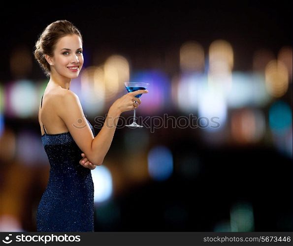 party, drinks, holidays, people and celebration concept - smiling woman in evening dress holding cocktail over night lights background
