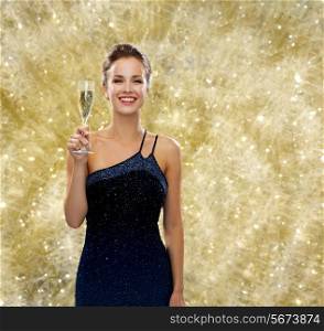 party, drinks, holidays, people and celebration concept - smiling woman in evening dress with glass of sparkling wine over yellow lights background