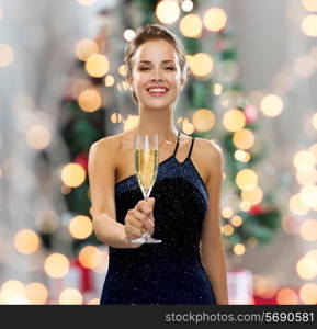 party, drinks, holidays, people and celebration concept - smiling woman in evening dress with glass of sparkling wine over christmas tree lights background