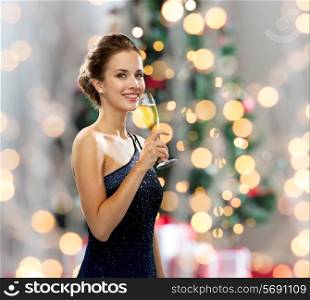 party, drinks, holidays, people and celebration concept - smiling woman in evening dress with glass of sparkling wine over christmas tree lights background