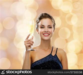 party, drinks, holidays, people and celebration concept - smiling woman in evening dress with glass of sparkling wine over beige lights background