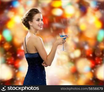 party, drinks, winter holidays, luxury and celebration concept - smiling woman in evening dress holding cocktail over red christmas lights background