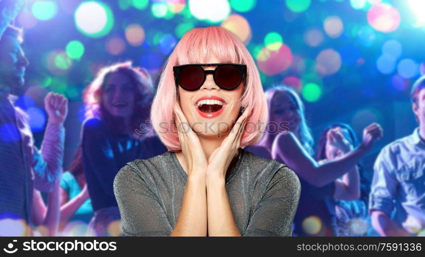 party, fashion and people concept - happy young woman in pink wig and black sunglasses over people dancing at nightclub background. happy woman in pink wig and sunglasses at party