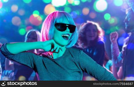 party, fashion and people concept - happy young woman in pink wig and black sunglasses over people dancing at nightclub background. woman in pink wig and sunglasses dancing at party