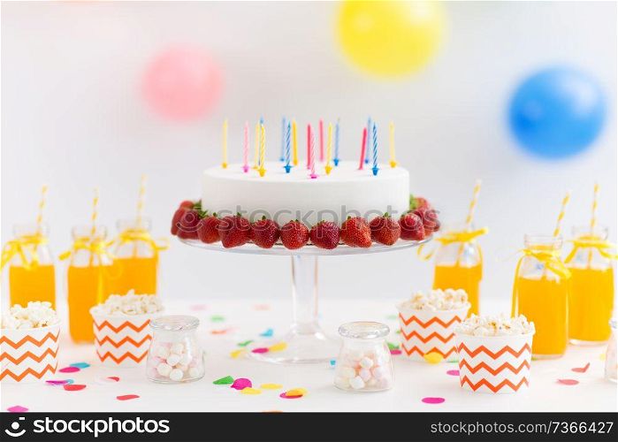 party food and festive concept - birthday cake with candles and strawberries, drinks, popcorn and marshmallow on table. birthday cake, juice, popcorn and marshmallow