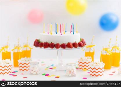 party food and festive concept - birthday cake with candles and strawberries, drinks, popcorn and marshmallow on table. birthday cake, juice, popcorn and marshmallow