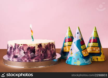 party hats cake with lighted candle desk against pink backdrop
